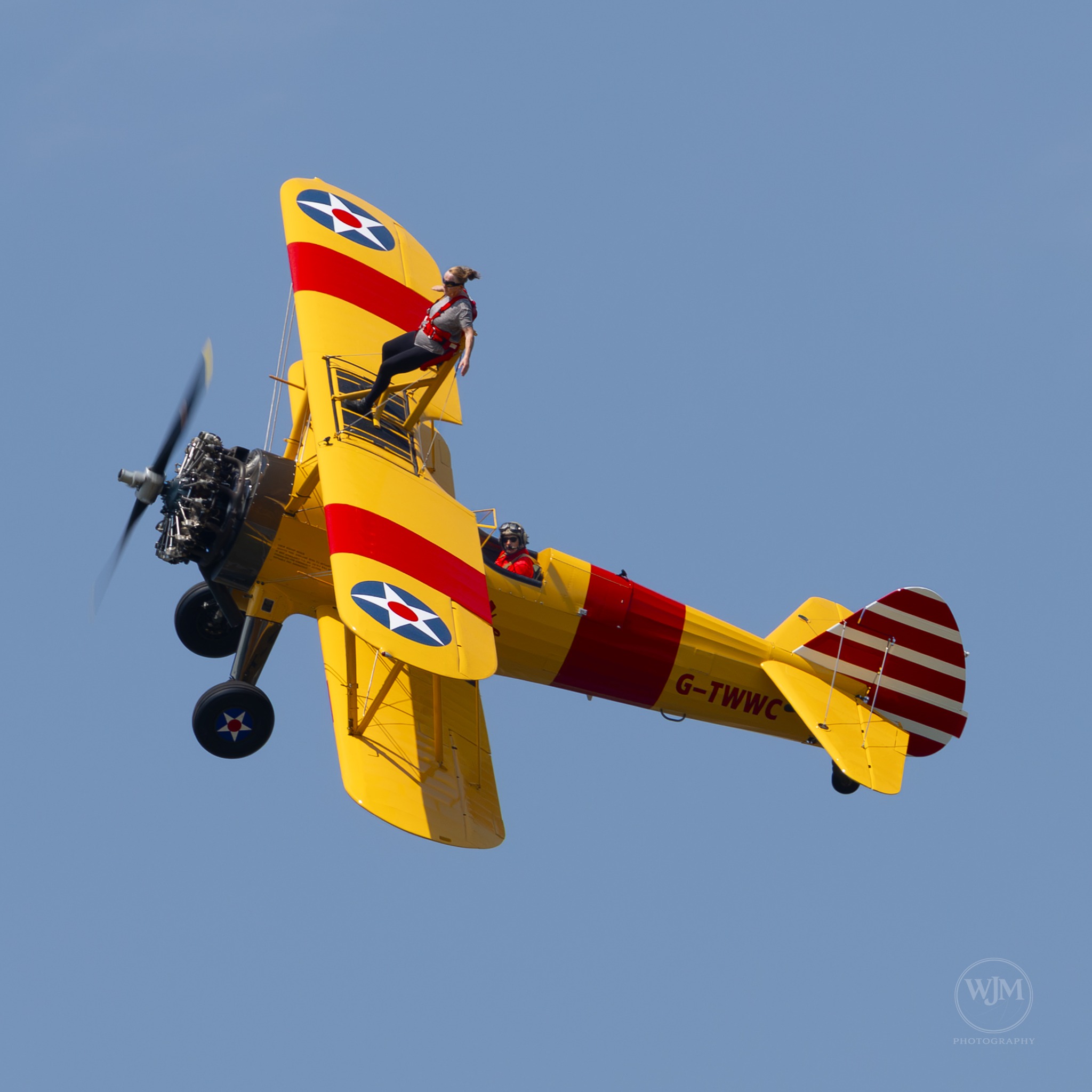 Wing walker on yellow Boeing Stearman aircraft against a blue sky